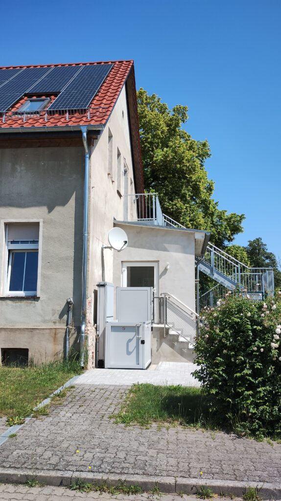 Seiteneingang eines Schullandheims mit Rollstuhullift für barrierefreien Zugang zum Haus, mit Solarzellen auf dem roten Zeigeldach des Hauses