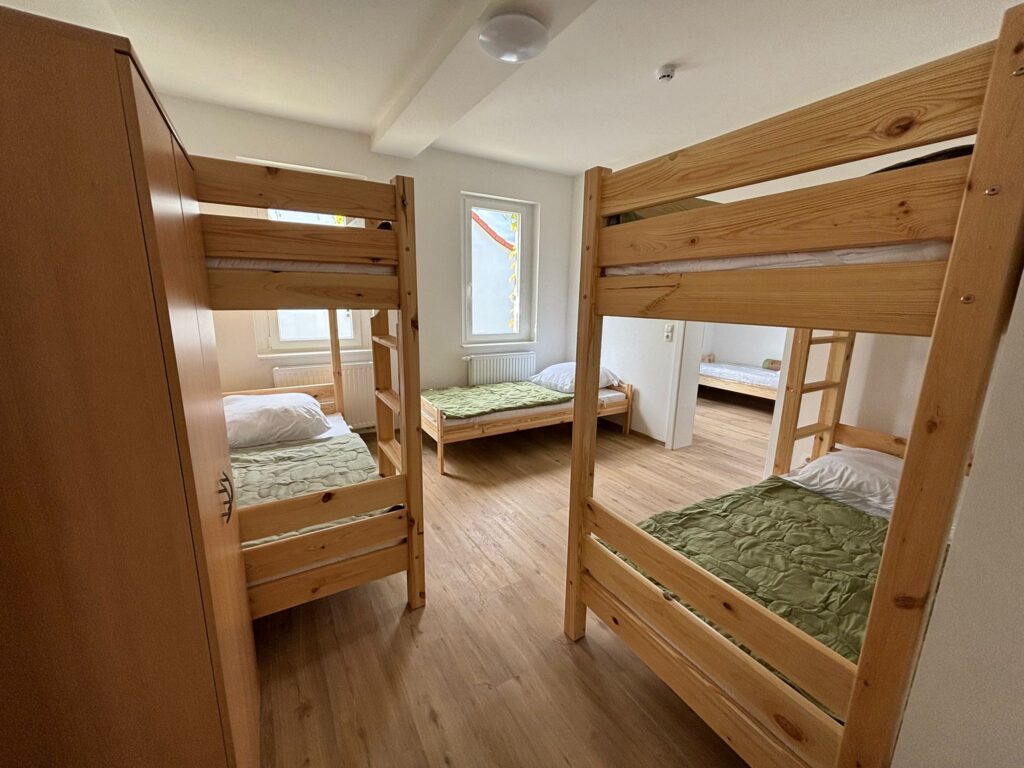 Modernes und helles Mehrbettzimmer mit Zwei Doppelstockbetten aus stabilem Holz und einem Einzelbett