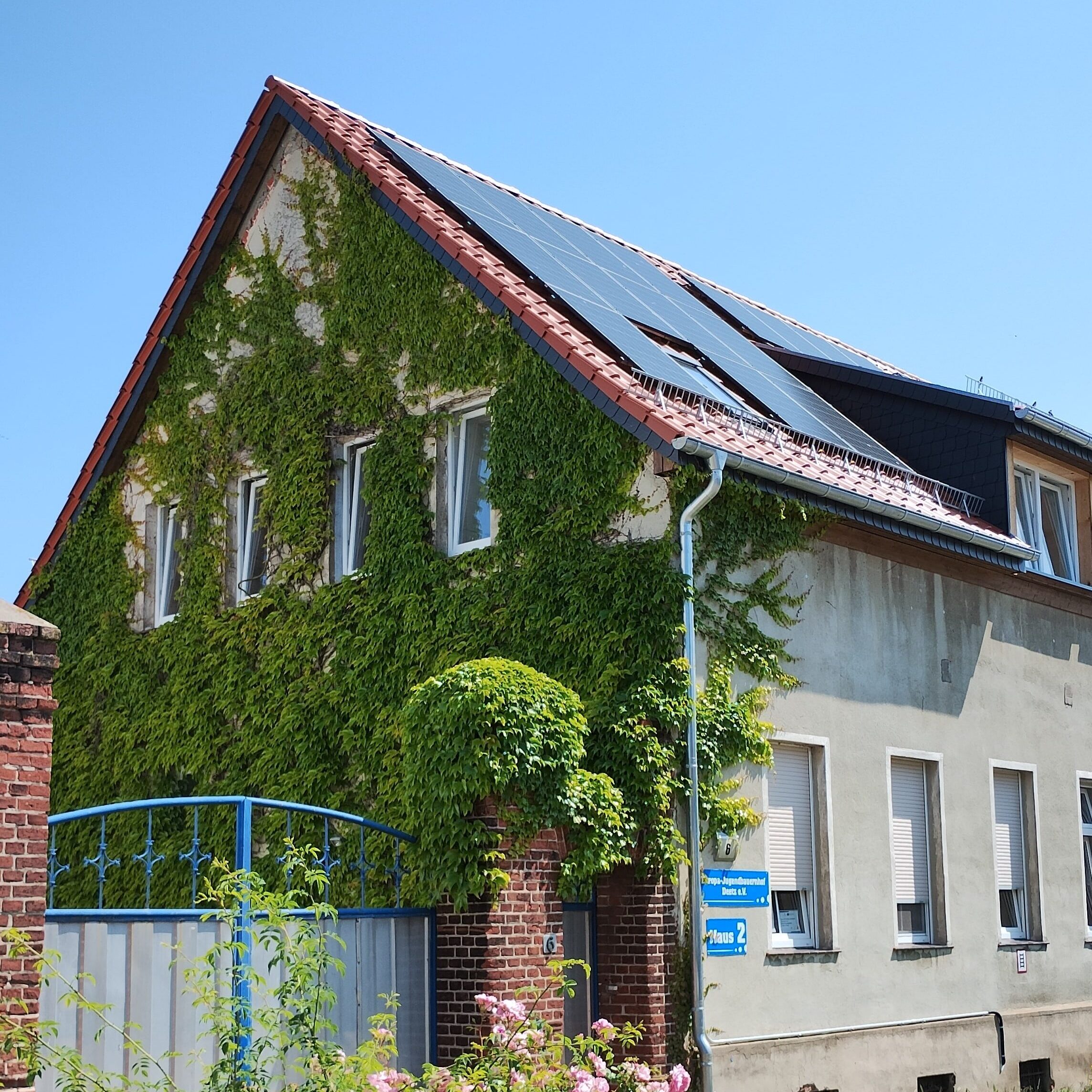 Haus eines Schullandheims, überwachsen mit grünem Efeu und Solarzellen auf rotem Ziegeldach