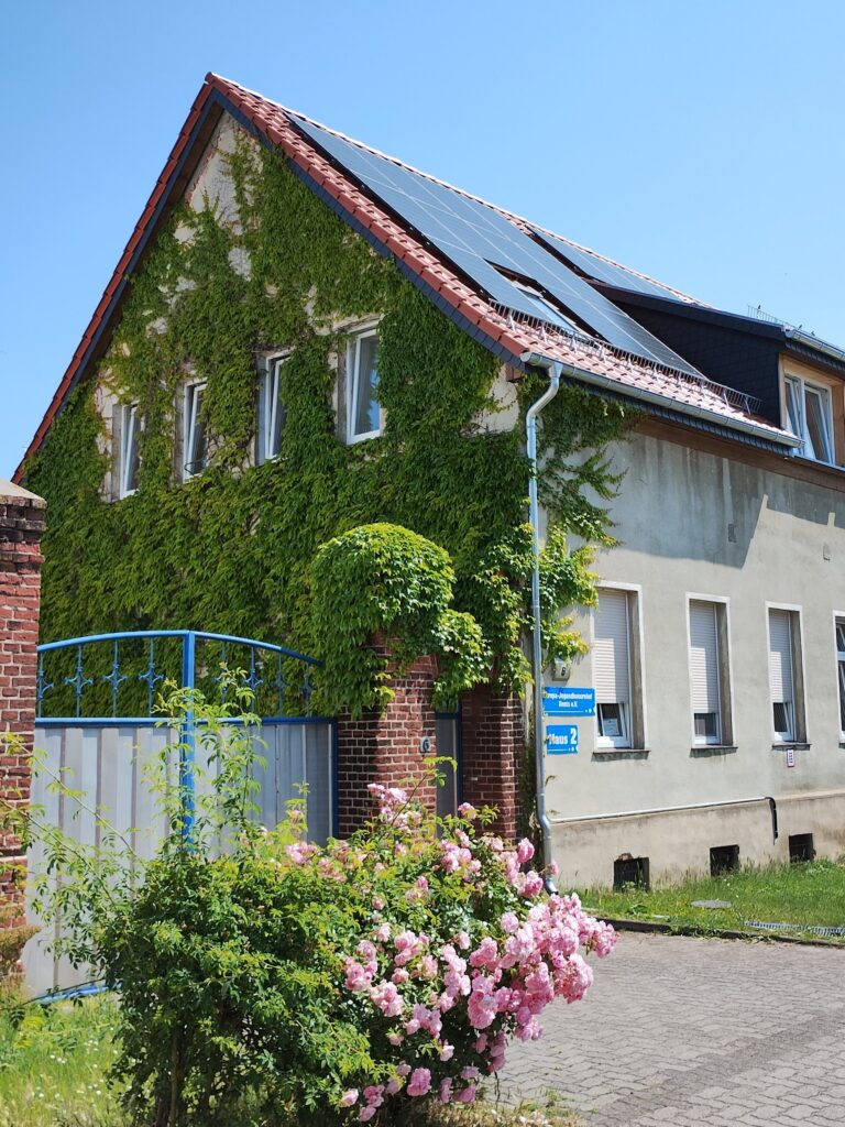 Haus eines Schullandheims, überwachsen mit grünem Efeu und Solarzellen auf rotem Ziegeldach